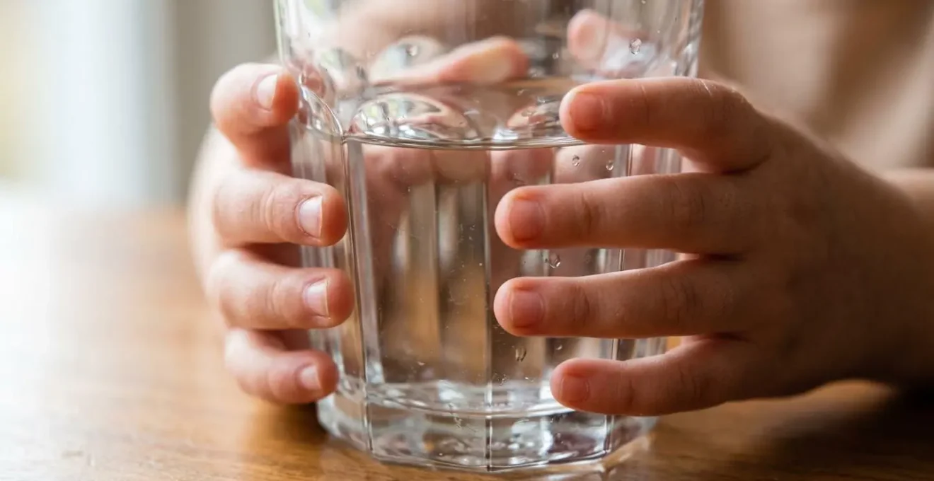 Enfant manipulant avec précaution un vrai verre en verre lors d'un repas, développant son autonomie