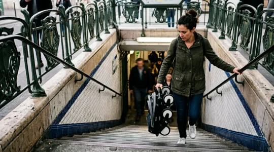 Parent gérant une poussette citadine dans les escaliers d'une station de métro parisienne