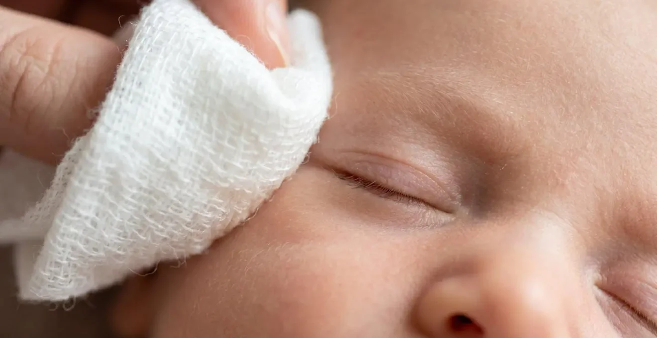 Gros plan sur une main tenant délicatement une compresse imbibée près de l'œil d'un bébé