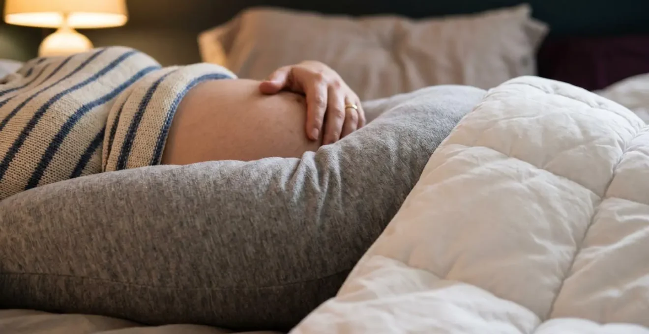 Femme enceinte allongée de profil, utilisant un coussin de grossesse avec la technique de calage optimal pour soutenir le ventre, les jambes et le dos.