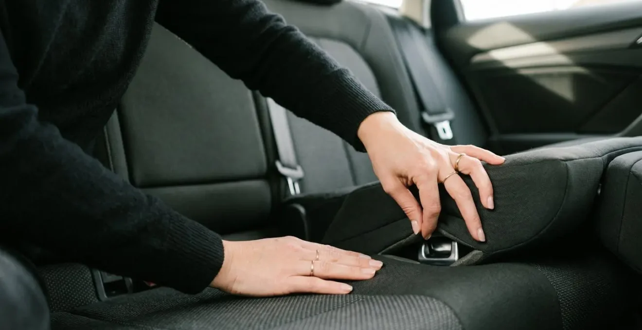 Mains utilisant la technique de la pince pour écarter délicatement les coussins de siège et révéler les ancrages Isofix